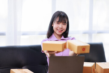 Obraz na płótnie Canvas Startup SME small business entrepreneur of freelance using a laptop with box, Asian business woman on sofa check online orders to prepare to pack the boxes sell to customers sme business ideas online.