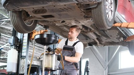 A young car mechanic changes the oil in the engine. Modern car service. Scheduled car diagnostics