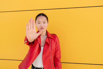 Young woman gesturing stop sign with hand in front of yellow wall