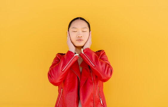 Young woman covering ears with hands against yellow background