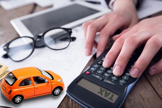 Hand working on calculator with car and pen on word tax. Concept of car tax.