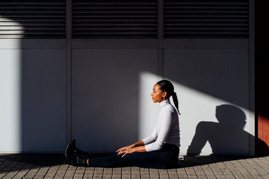 Young businesswoman sitting by wall on footpath