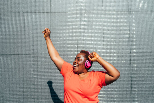 Happy woman enjoying music dancing with hand raised in front of wall