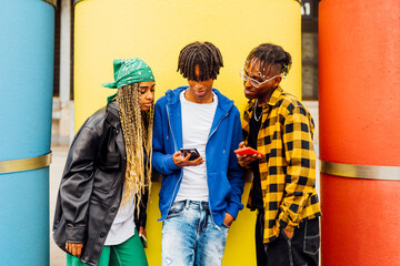 Young man sharing smart phone with friends in front of yellow pipe