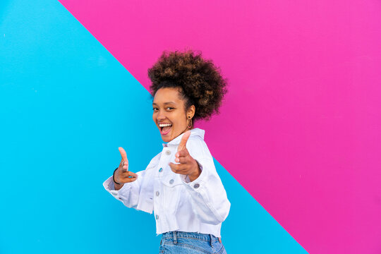 Cheerful woman with Afro hairstyle gesturing in front of pink and blue wall