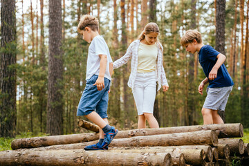 Group of three children balancing on tree trunks at forest.