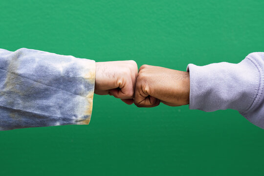 Hands of friends bumping fists in front of green wall