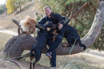 A man and his pets. An adult male sitting on the trunk of a pine tree.