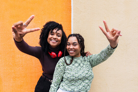 Smiling women gesturing peace sign in front of wall