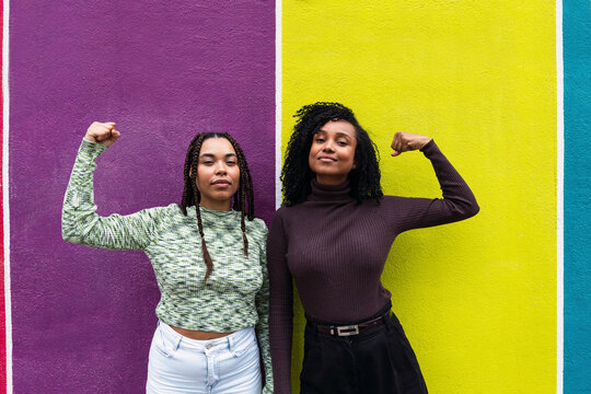 Smiling friends flexing muscles in front of wall
