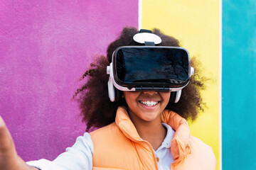 Smiling girl wearing virtual reality simulator standing in front of multi colored wall