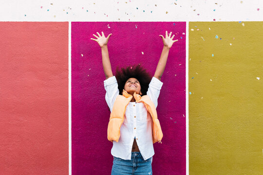 Girl with arms raised throwing confetti standing in front of colorful wall