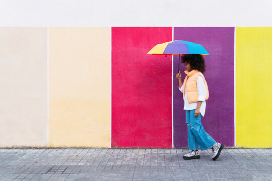 Girl walking with multi colored umbrella on footpath