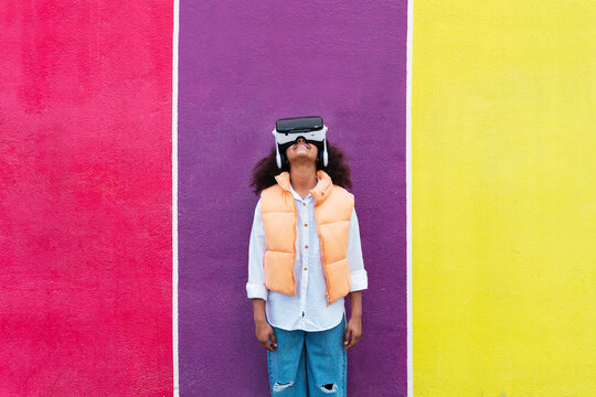 Smiling girl wearing virtual reality simulator in front of multi colored wall