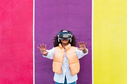 Girl wearing virtual reality simulator gesturing in front of colorful wall