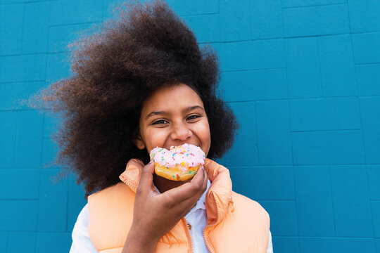 Smiling girl eating doughnut in front of blue wall