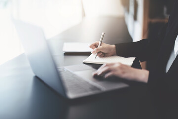 usiness woman writing marketing plan in notebook ready to use computer in office