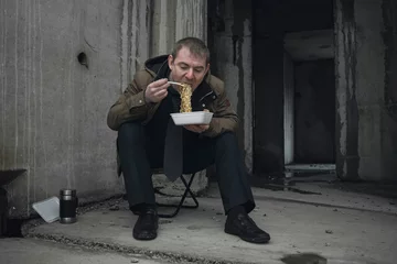 Fotobehang A bankrupt and homeless businessman is forced to eat cheap food in an abandoned building. The concept of losing money and ruin © Николай Чекалин
