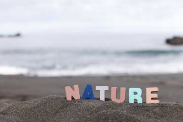 Word nature made of colourful wooden letters stand on the beach in front of the ocean.