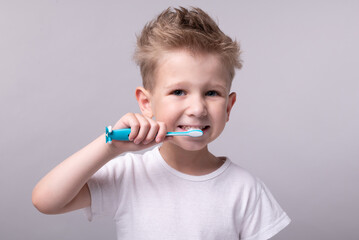 a boy in a white t-shirt brushes his teeth with a toothbrush