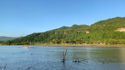 The landscape of the river with clear blue sky and mountains. The traditional fishing boat crosses the river from the distance
