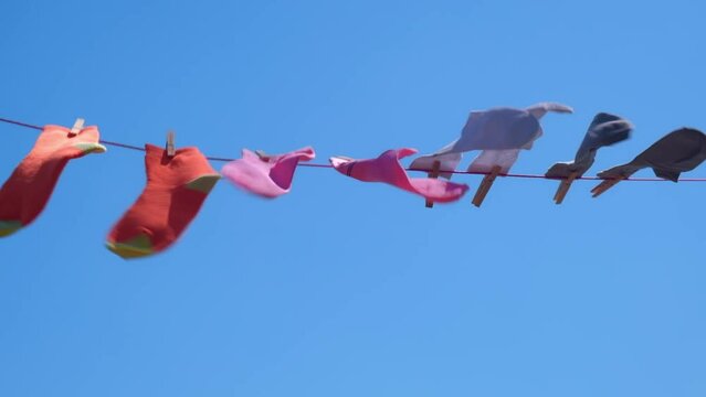 clean colored socks for men and women are dried on a rope with clothespins after washing. the wind shakes bright unisex socks against the blue sky on a sunny summer day. slow motion.