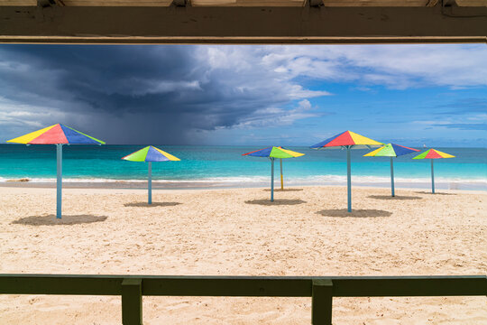 Multicolored striped umbrellas on white sand beach under storm clouds, Antigua, West Indies, Caribbean