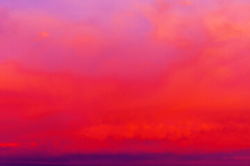 Clouds illuminated by the setting sun. Red sunset in the evening sky. Colorful dramatic view with red and purple clouds.