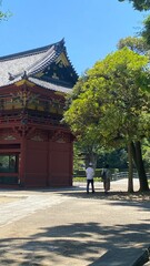 Fototapeta premium Colorful “Romon” two story high tower gate of “Nezu” shrine with zen garden pond bridge in the back as entry, beautiful summer sunlight and historic scenery with people, year 2022 June 28th