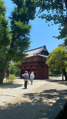 Colorful “Romon” two story high tower gate of “Nezu” shrine with zen garden pond bridge in the back as entry, beautiful summer sunlight and historic scenery with people, year 2022 June 28th