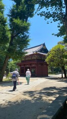 Colorful “Romon” two story high tower gate of “Nezu” shrine with zen garden pond bridge in the back as entry, beautiful summer sunlight and historic scenery with people, year 2022 June 28th