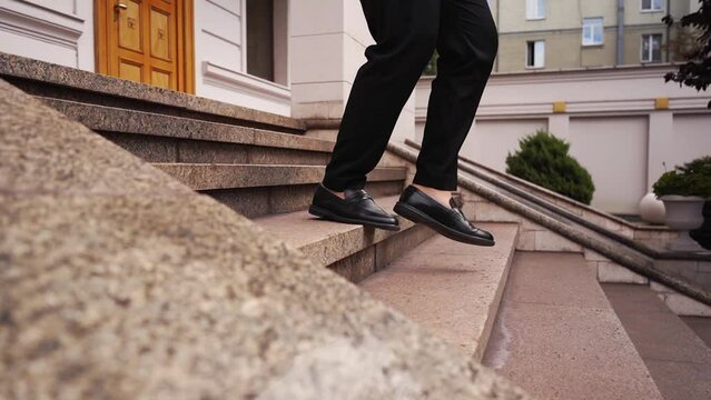 Close up shot of hurry businessman in black formal suit feet in loafer's shoes walking down marble stairs of luxury house outdoors. Man goes down stairs of stone from office in shoes on bare feet.