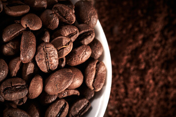 Roasted coffee whole and ground beans in bowl isolated close up on brown grunge background