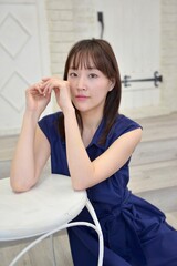 室内で椅子にもたれポーズをとるワンピース姿の清楚な若い女性	
