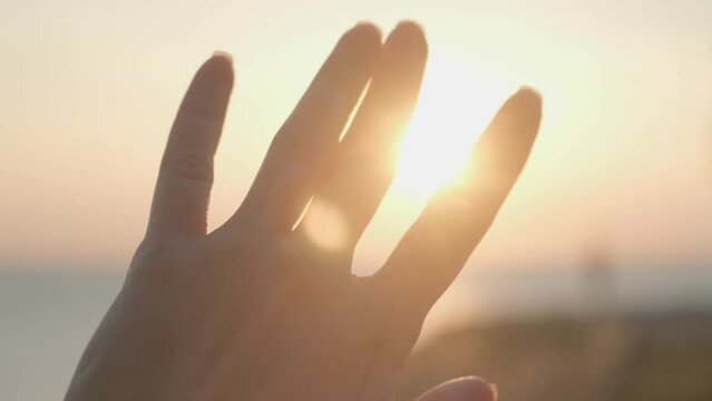 female hand touching the sun, woman hand moving fingers against sunlight, sunlight shining through fingers.