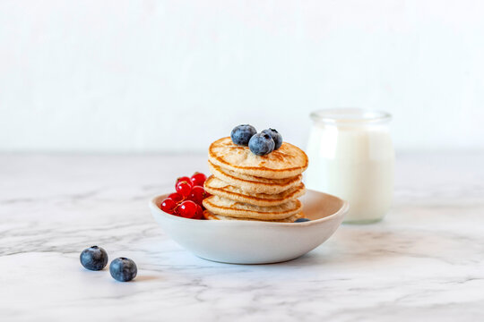 Homemade mini pancakes served with blueberries and red currants and joghurt