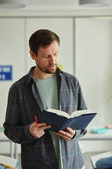 Vertical portrait of bearded male teacher holding book while explaining topic in class