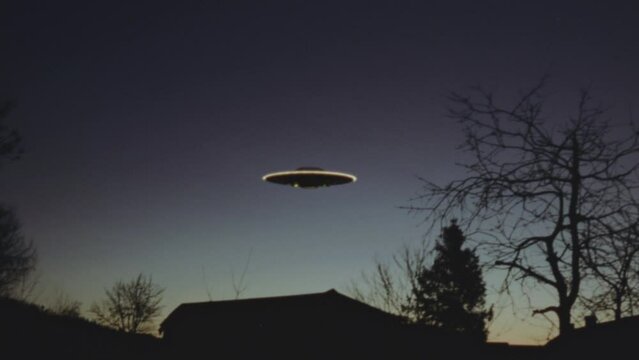 Handheld, grainy footage of UFO flying over houses at dusk.