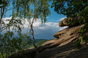 Rocky cliff with trees growing, mountanins and beautiful blue sky in the background. Summer vacations and travel destination
