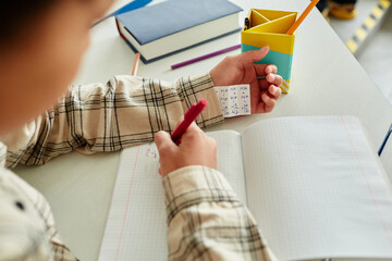 Close up of unrecognizable young boy cheating during test in school and hiding note in sleeve, copy space - Powered by Adobe