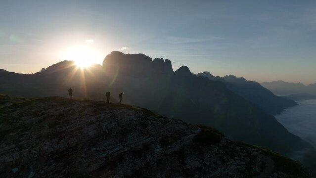 Female and male hikers at the top of the mountain at sunrise. Beautiful Morning at Tre Cime di Lavaredo mountains with blue sky, Dolomites Alps, Italy.