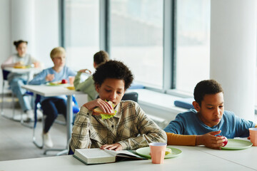 Portrait of schoolchildren at lunch break, focus on young african American girl eating sandwich and...