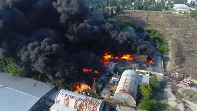 Rocket attack on the plant. Warehouse building strong fire in warehouses black smoke and fire. Shooting from a drone over a large-scale fire. Grain video. Rescuers put out a huge fire