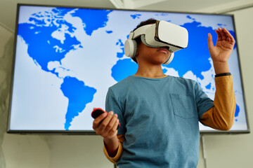 Waist up portrait of young black boy using VR technology in school classroom with geography map in...