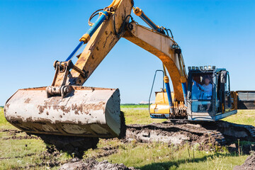 An excavator with a wide bucket removes a layer of fertile soil. Preparatory work for digging a pit. Earth-moving equipment and earthworks.