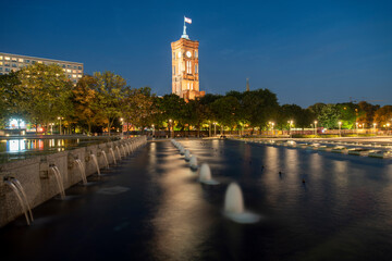 Fototapeta premium Fountain on Alexanderplatz by the Tv Tower Fernsehturm and the Red City hall ( Rotes Rathaus) in the background at night, Berlin, Germany
