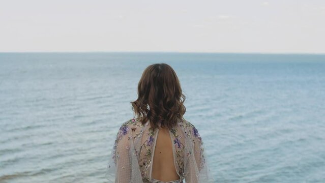 A woman admires the sea where white clouds merge with the water on the horizon. slow motion. Rear view
