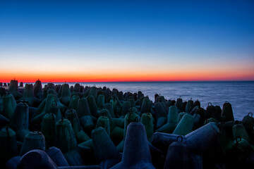 Fototapeta Gwiazdobloki chroniące falochron nadmorski. Zachód słońca przy umocnieniach brzegu morskiego obraz