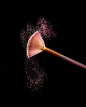 Make up brush with cosmetic powder splash, over black background. Splash image