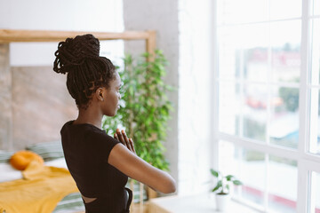 Rearview mindful and meditating young multicultural woman in black sportswear practicing yoga...